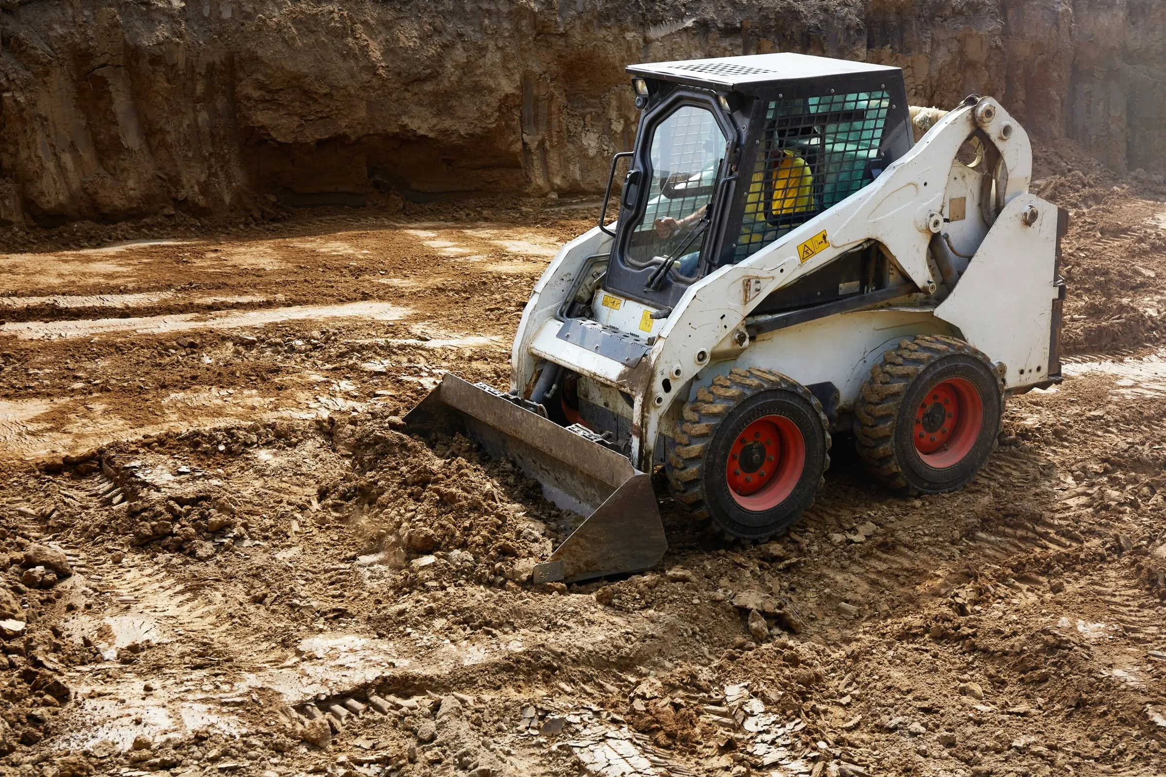 A white skid steer loader clearing mud and earth on a dirt construction site.